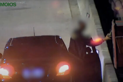 Motorista fora do carro tenta mexer no equipamento de cobrança em uma cabine de pedágio da rodovia Tamoios durante a noite.