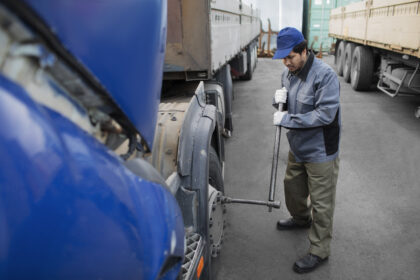 Homem usando ferramenta realiza manutenção na roda de caminhão em pátio de veículos