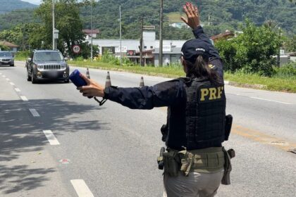 Agente da PRF estende o braço para sinalizar parada de veículo em rodovia.