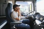 Tired of work. Sitting in the cabin. Young african american truck driver is with his vehicle at daytime