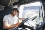 African American truck driver is sitting behind the wheel holding a clipboard and checking the documents for the cargo