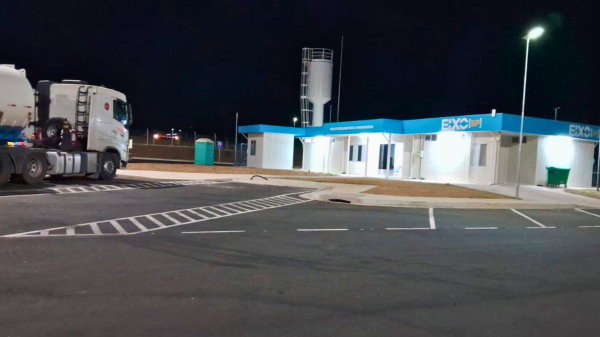 Área de estacionamento noturno em Ponto de Parada e Descanso, com caminhão estacionado e prédio iluminado ao fundo.