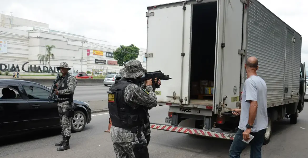 Policiais armados inspecionam caminhão de carga em operação de fiscalização nas rodovias.