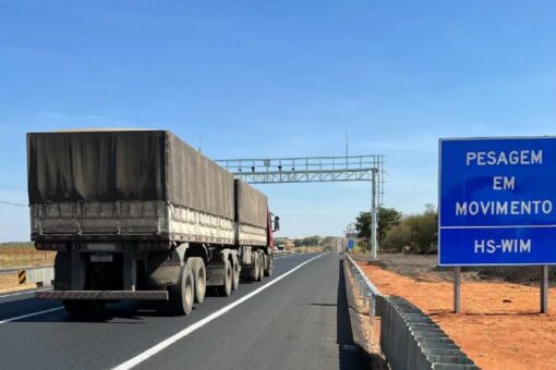 Caminhão em rodovia passando por sistema de pesagem em movimento indicado por placa azul.