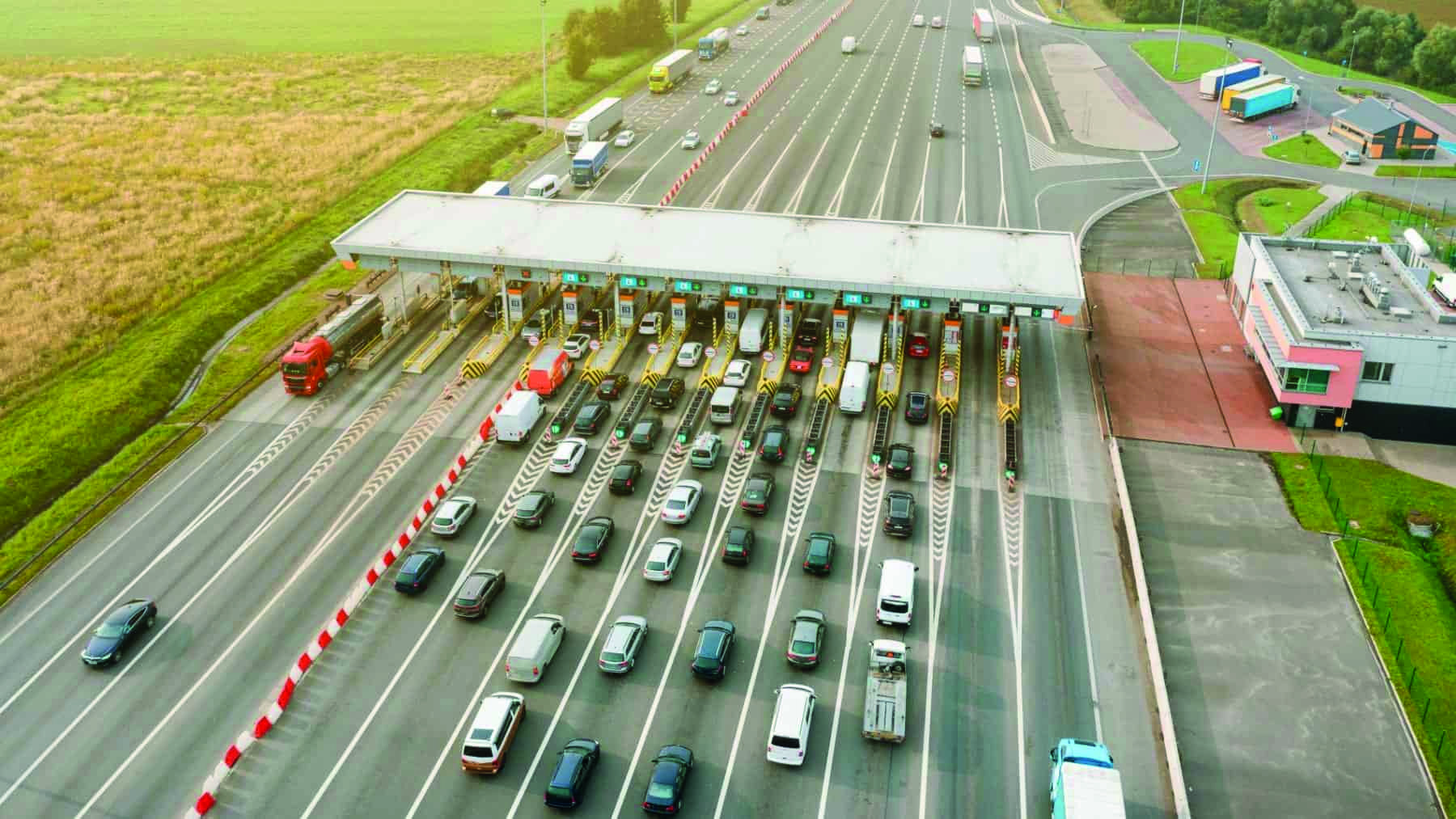 Vista aérea de uma praça de pedágio movimentada com caminhões e carros, representando o impacto das novas exigências de seguro nas concessões rodoviárias e nos valores de pedágio.