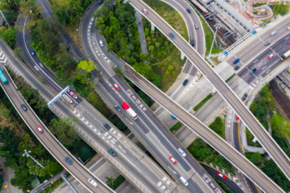 Vista aérea de um complexo viário com várias pistas e viadutos entrelaçados, com carros circulando e áreas verdes ao redor.