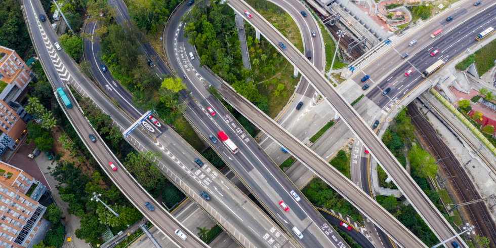 Vista aérea de um complexo viário com várias pistas e viadutos entrelaçados, com carros circulando e áreas verdes ao redor.