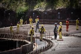 Operários com capacetes e uniformes de proteção atuam em área de obras após desabamento.