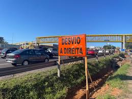 Placa laranja de sinalização com os dizeres “Desvio à direita” instalada às margens de uma estrada, com um carro passando ao fundo.