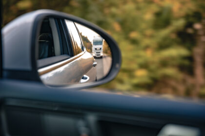 Retrovisor de carro reflete trânsito em rodovia, com veículos ao fundo e mensagem informativa em destaque.