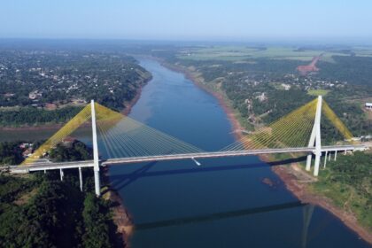 Vista aérea de uma ponte estaiada atravessando um rio largo, com cabos amarelos e vegetação nas margens.