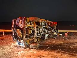 Caminhão tombado à noite apresenta estrutura retorcida e carga exposta após acidente na rodovia.