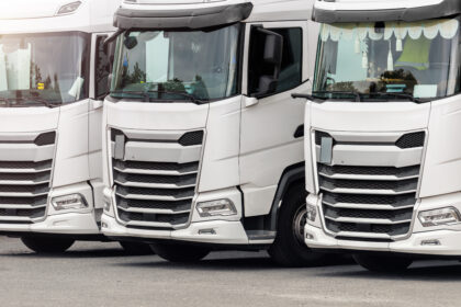 Frota de caminhões brancos modernos estacionados lado a lado, vistos de frente, em área pavimentada.