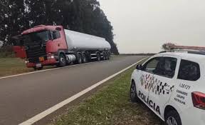 Caminhão-tanque parado no acostamento de rodovia enquanto viatura da Polícia Rodoviária Federal faz fiscalização.