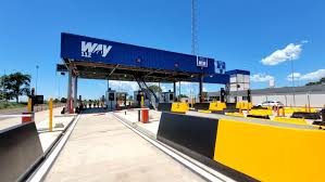 Posto de pedágio com cobertura azul, área ampla de abastecimento e barreiras amarelas e pretas na entrada.