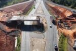 Vista aérea de viaduto e obras sobre rodovia, com carros circulando e obras nas laterais.