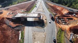 Vista aérea de viaduto e obras sobre rodovia, com carros circulando e obras nas laterais.
