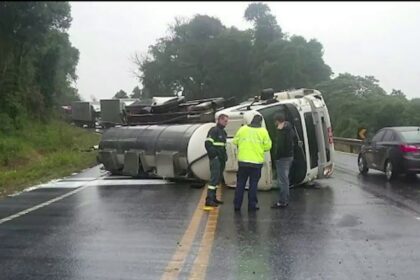 Acidente entre veículos em rodovia molhada, com carros danificados e agentes usando coletes refletivos no local.