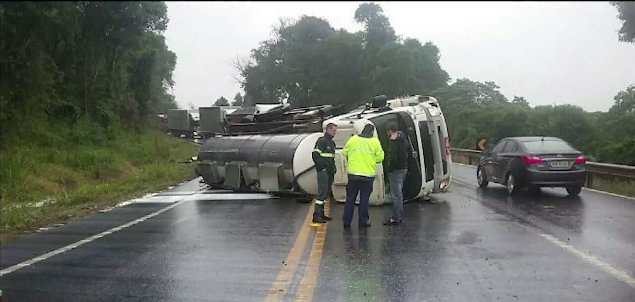 Acidente entre veículos em rodovia molhada, com carros danificados e agentes usando coletes refletivos no local.