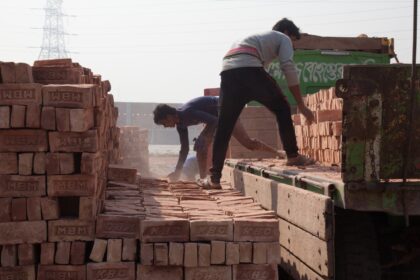 Pessoas movimentam tijolos junto à carroceria de um caminhão, ao lado de pilhas do material